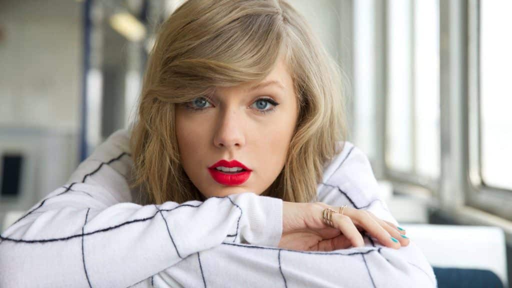 La cantante Taylor Swift con los labios pintados de rojo y una camisa a cuadros.