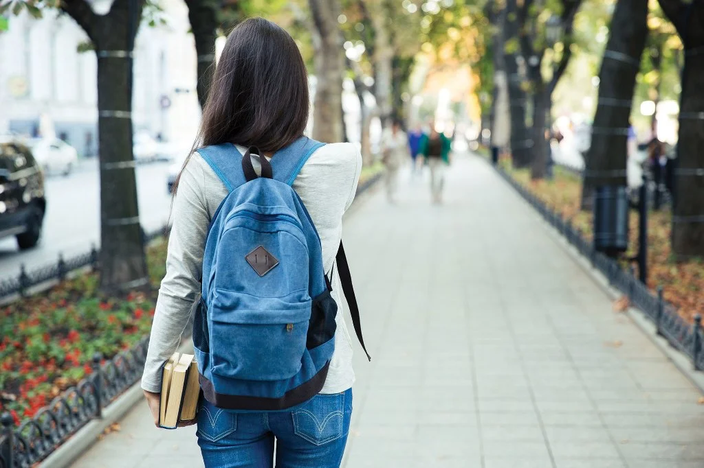 Joven caminando por una calle con una mochila azul en la espalda