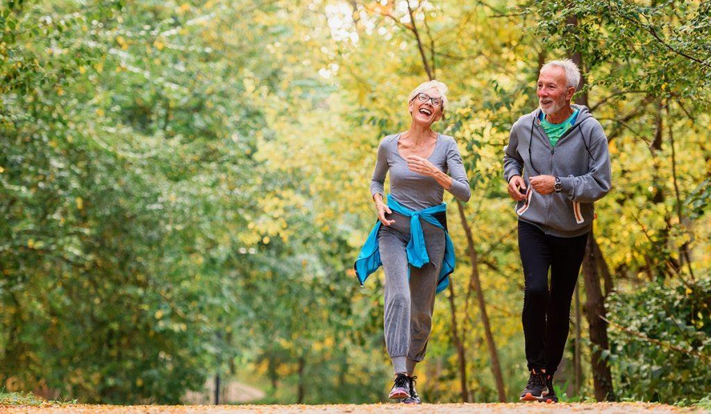 Dos personas mayores corriendo en el bosque donde se estan divirtiendo.